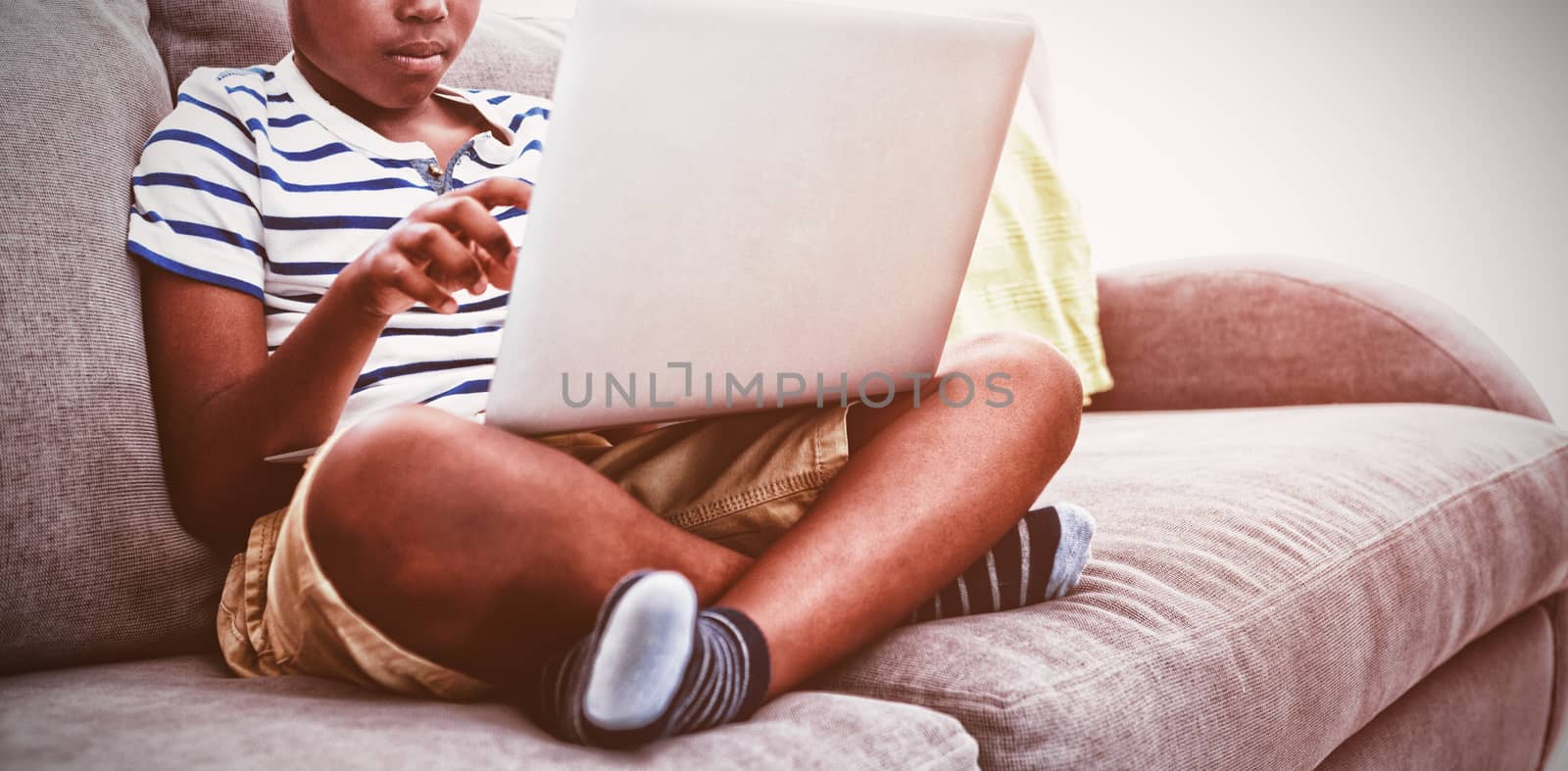 Boy using laptop while sitting with crossed legged on sofa in living room at home