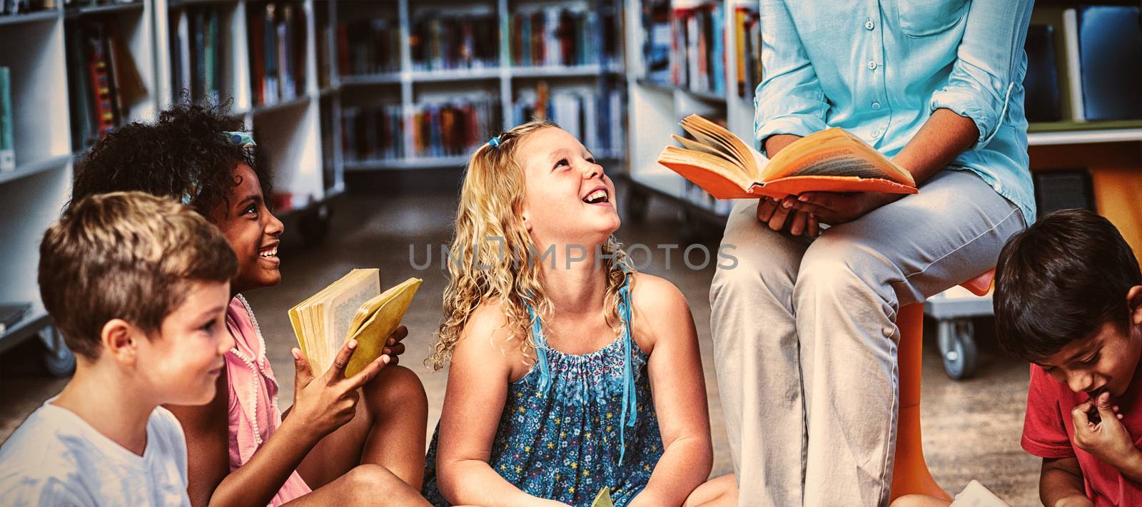 Low section of female teacher with smiling children reading books in library