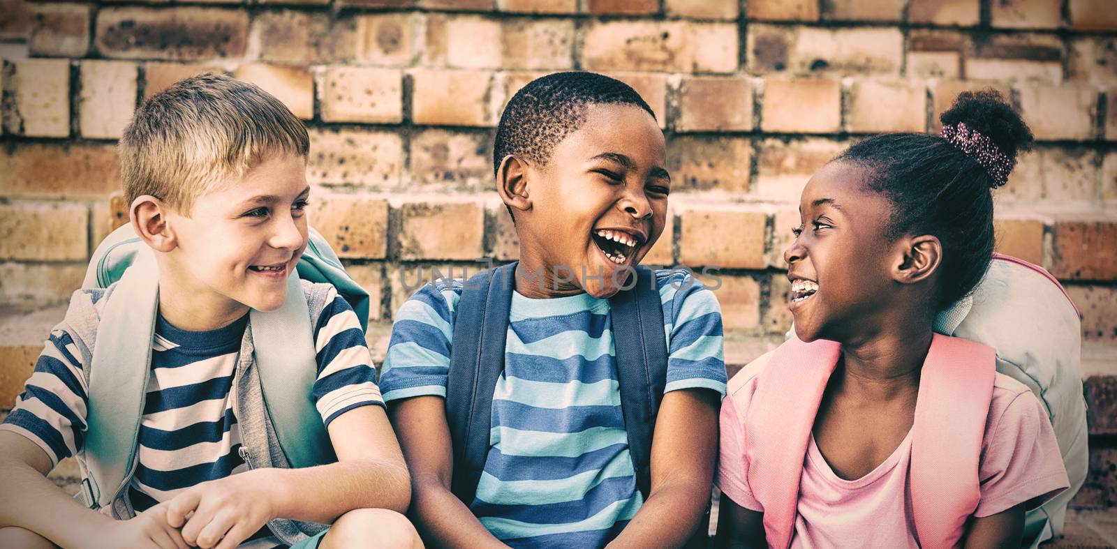 Happy children with backpacks sitting on steps at school