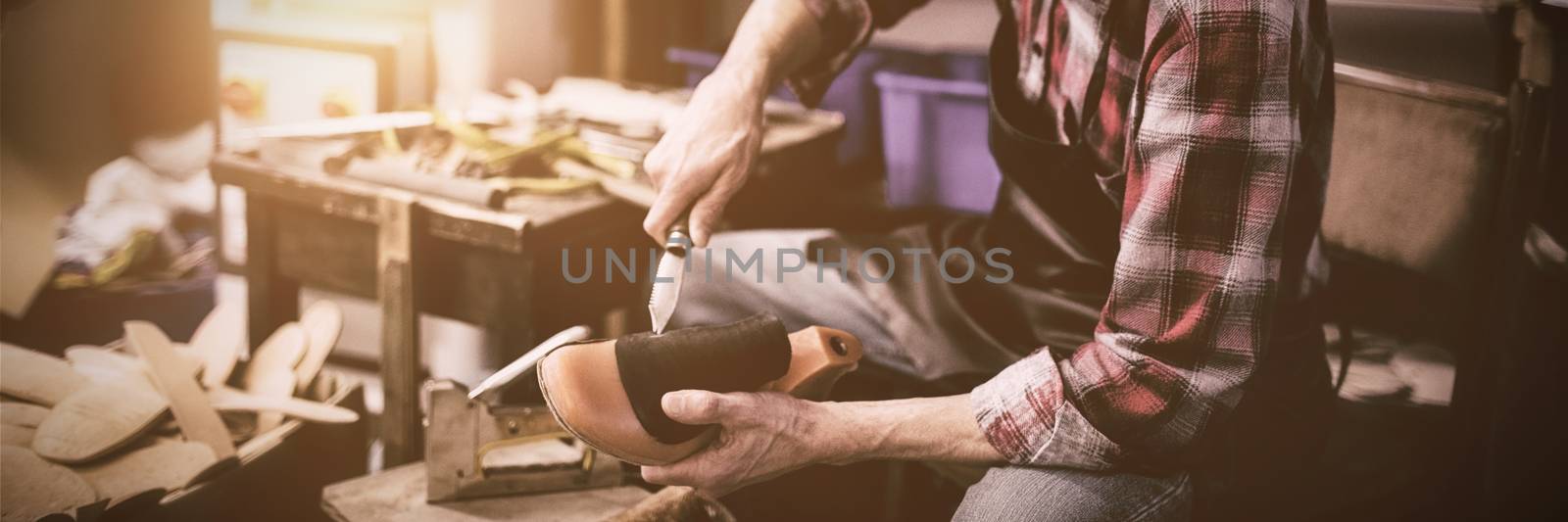Cobbler holding a knife and a shoe in his workshop