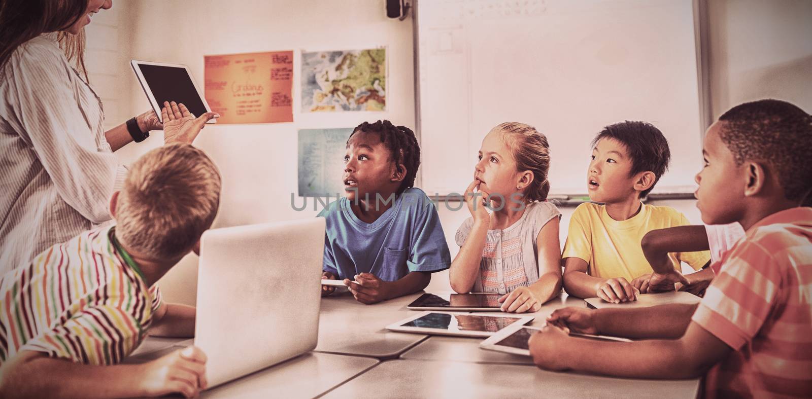 Pupils listening to teacher showing digital tablet in classroom