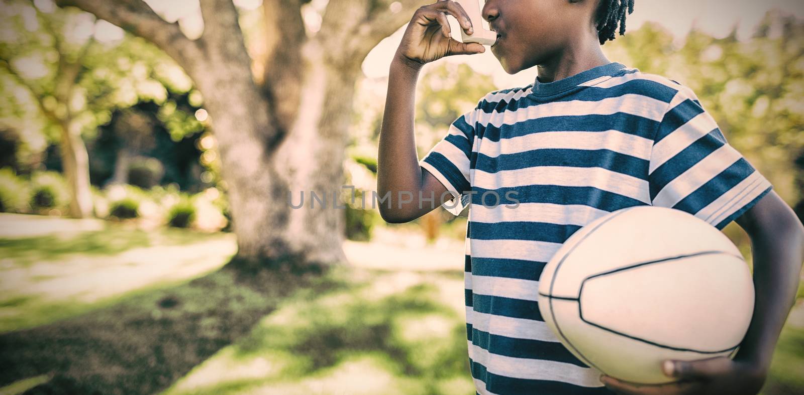 Boy using asthma inhaler in the park on a sunny day