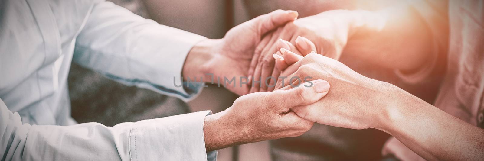 Midsection of therapist holding patient hands on sofa at home