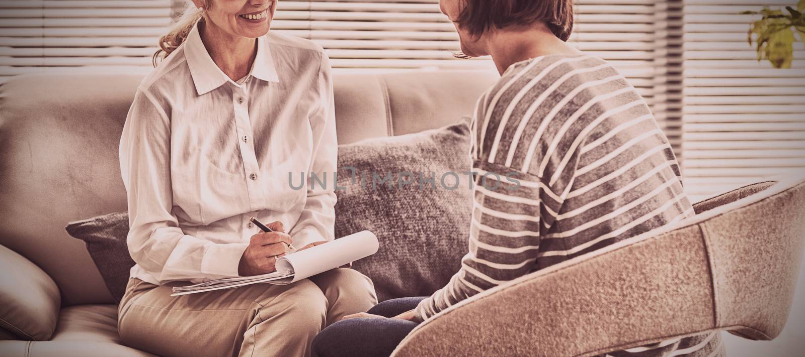 Smiling therapist with woman on sofa at home