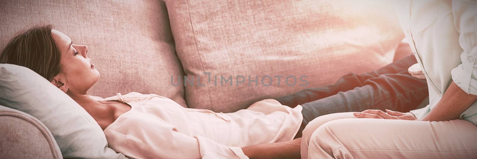 Hypnotherapist holding pendulum by patient on sofa at home