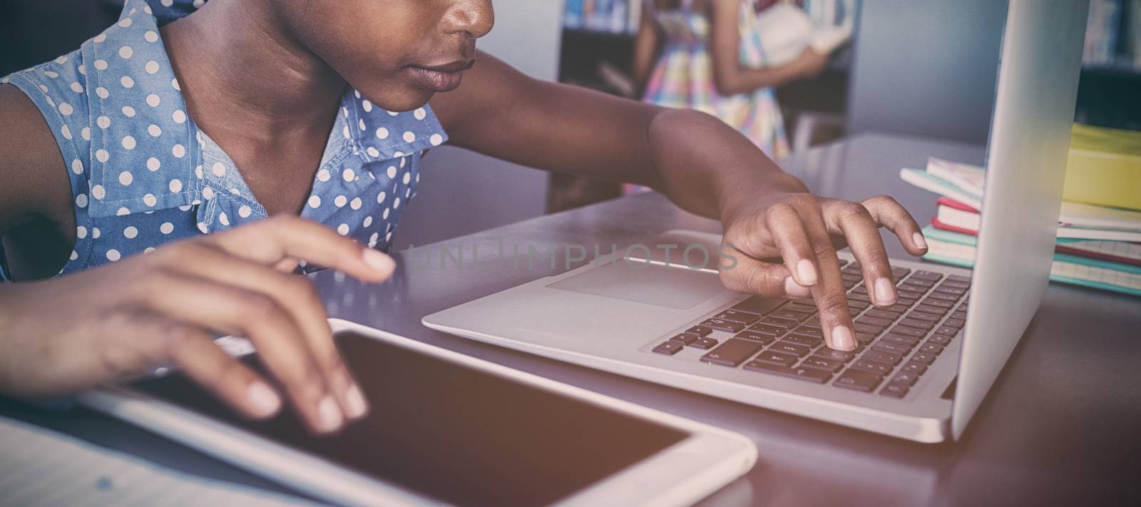 Girl using tablet computer and laptop while sitting at desk in library