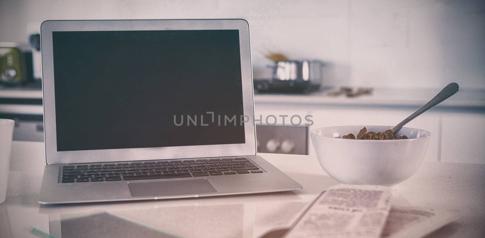 Breakfast bowl with coffee mug, laptop and newspaper in kitchen by Wavebreakmedia