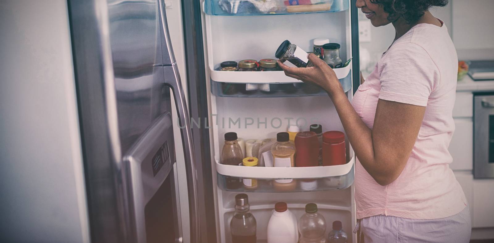 Woman removing bottle from refrigerator in kitchen by Wavebreakmedia