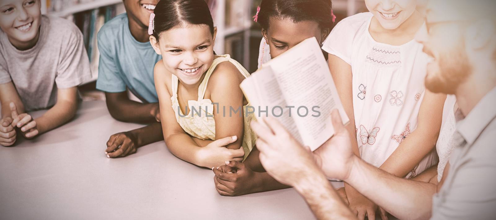 Male teacher with book teaching students in library at school