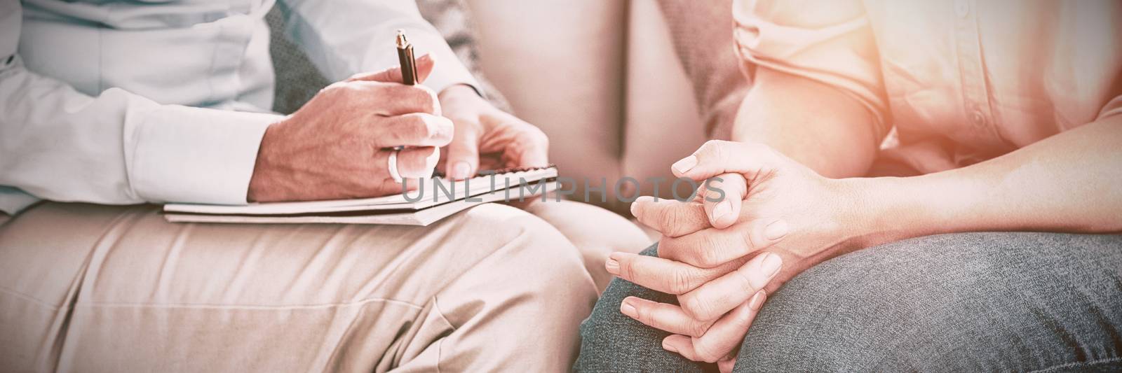 Midsection of therapist with patient on sofa at home