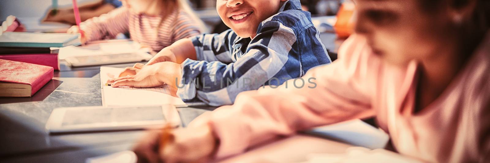 Portrait of smiling schoolboy doing his homework in classroom by Wavebreakmedia
