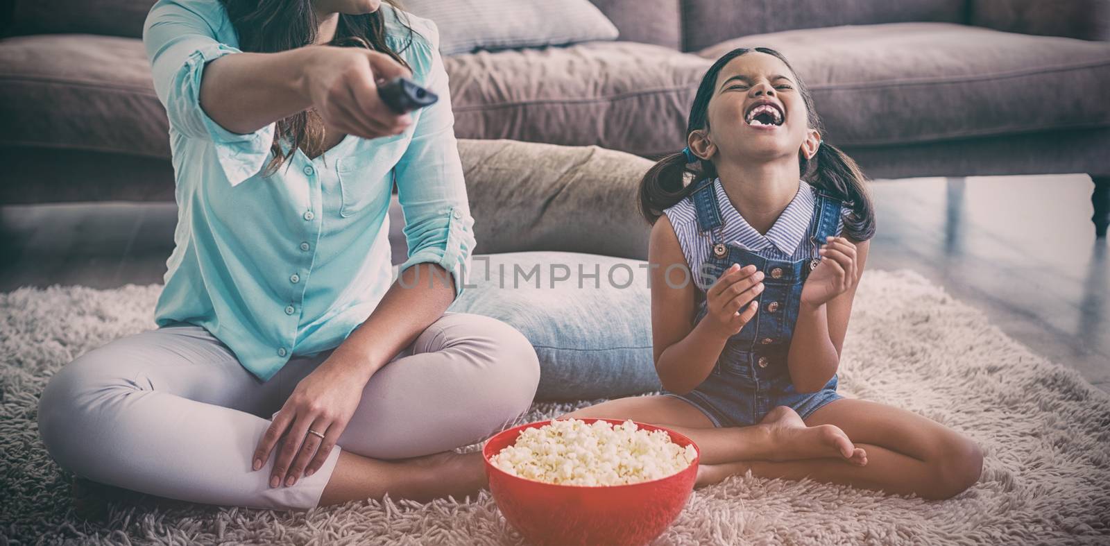 Mother and daughter watching television while having popcorn in living room at home