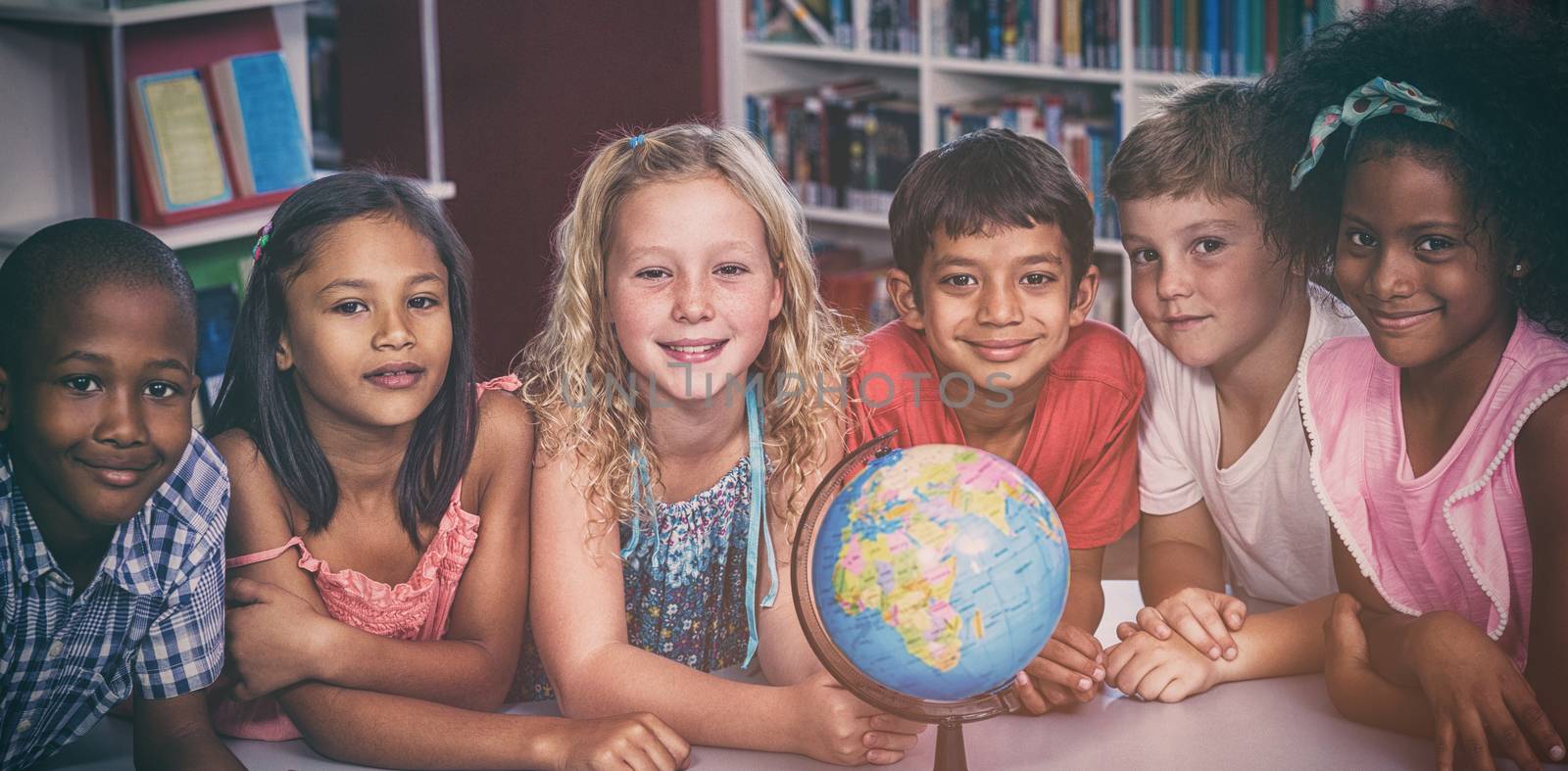 Portrait of smiling children with globe on table in library 