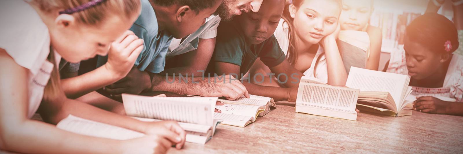 Teacher and kids lying on floor reading book in library by Wavebreakmedia