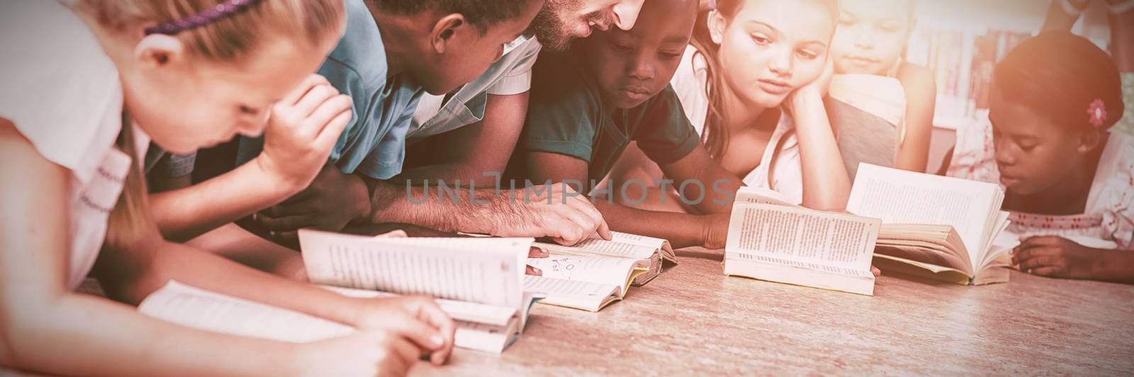 Teacher and kids lying on floor reading book in library at elementary school