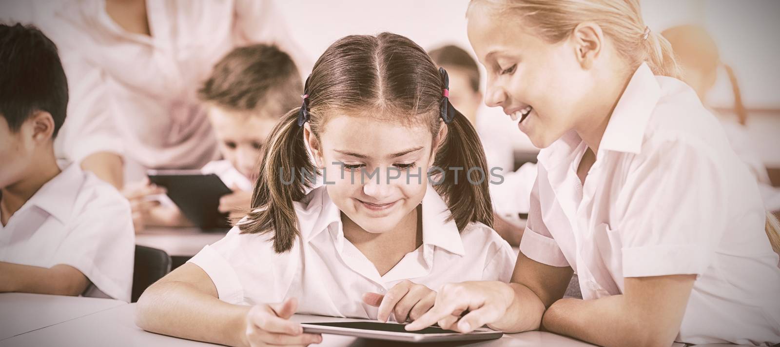 Smiling children using digital tablets in classroom at school