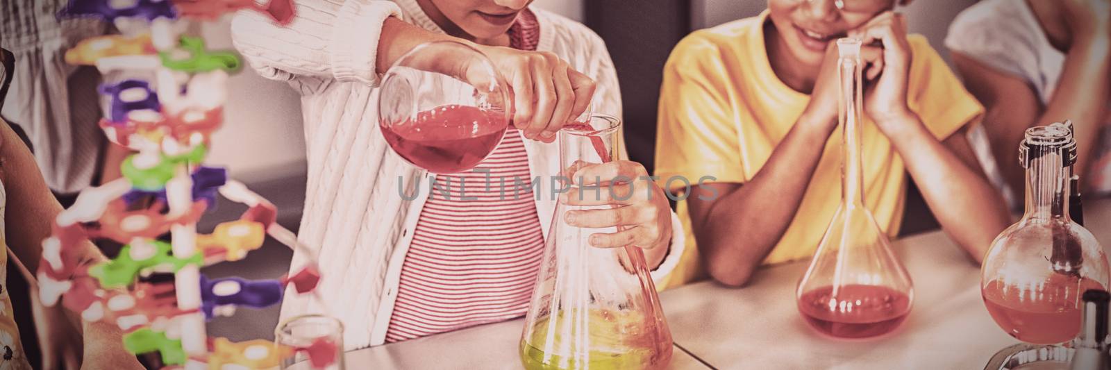 Pupil doing science while classmates looking her in classroom