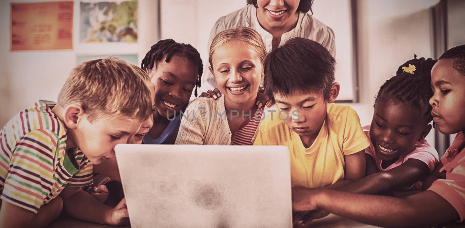 Happy teacher and pupils using laptop in classroom at school