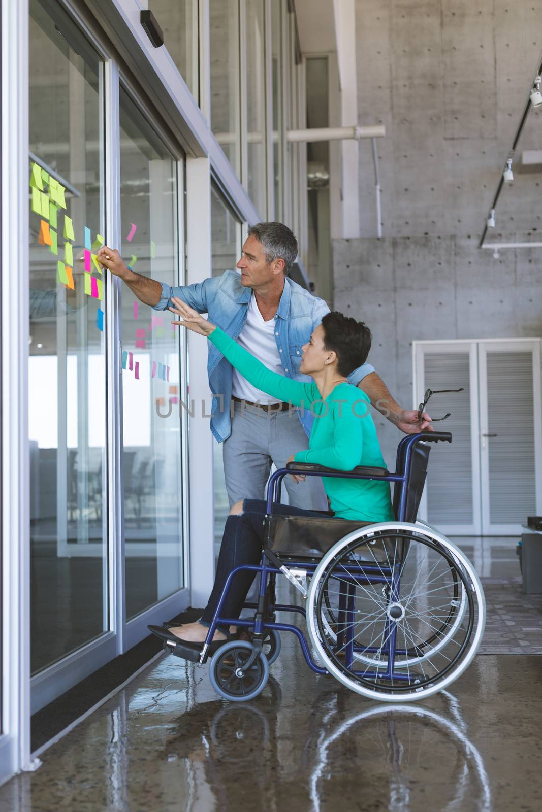 Side vie of business people discussing over sticky notes on glass wall in office