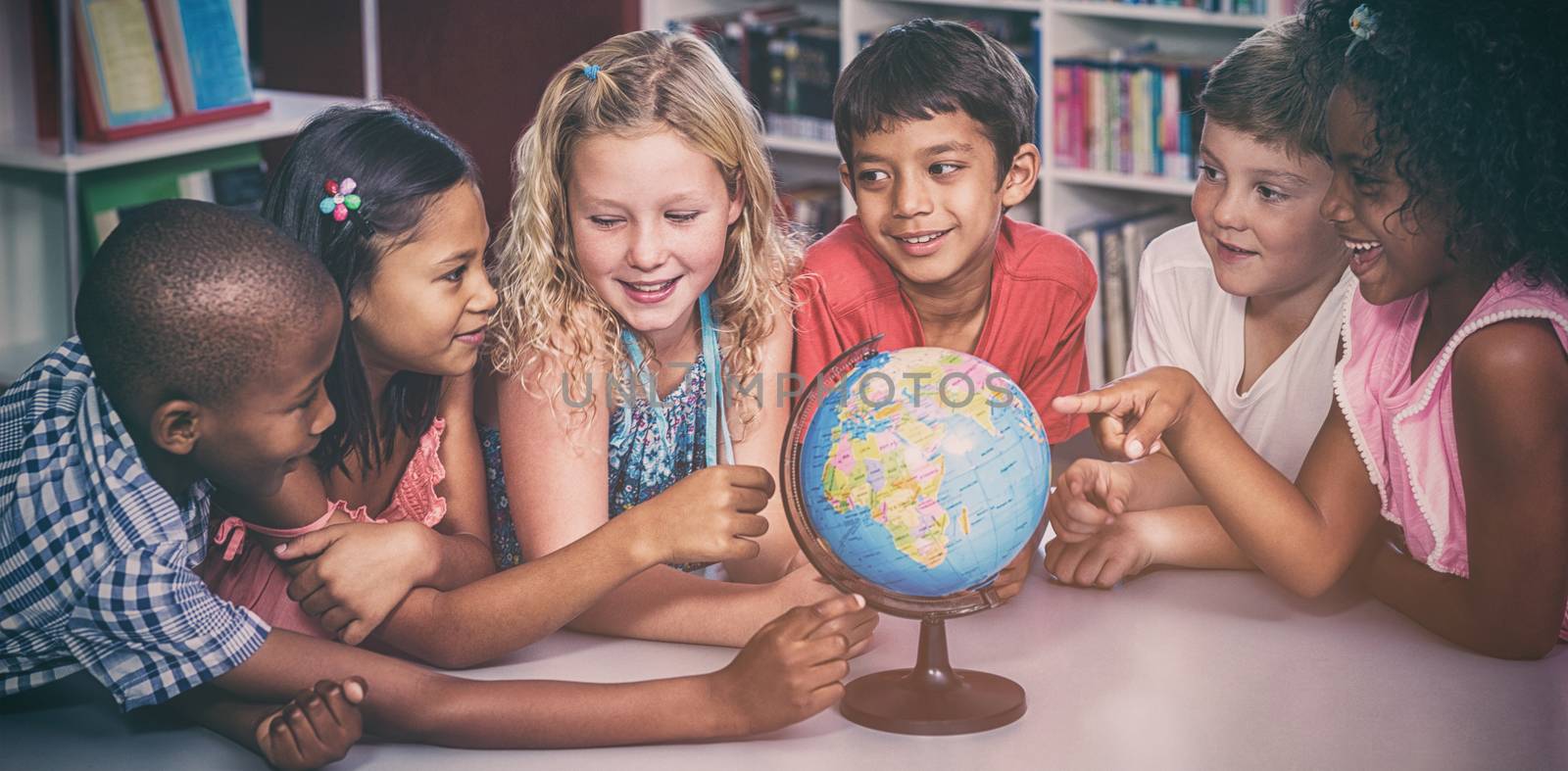 Smiling children with globe on table in library 