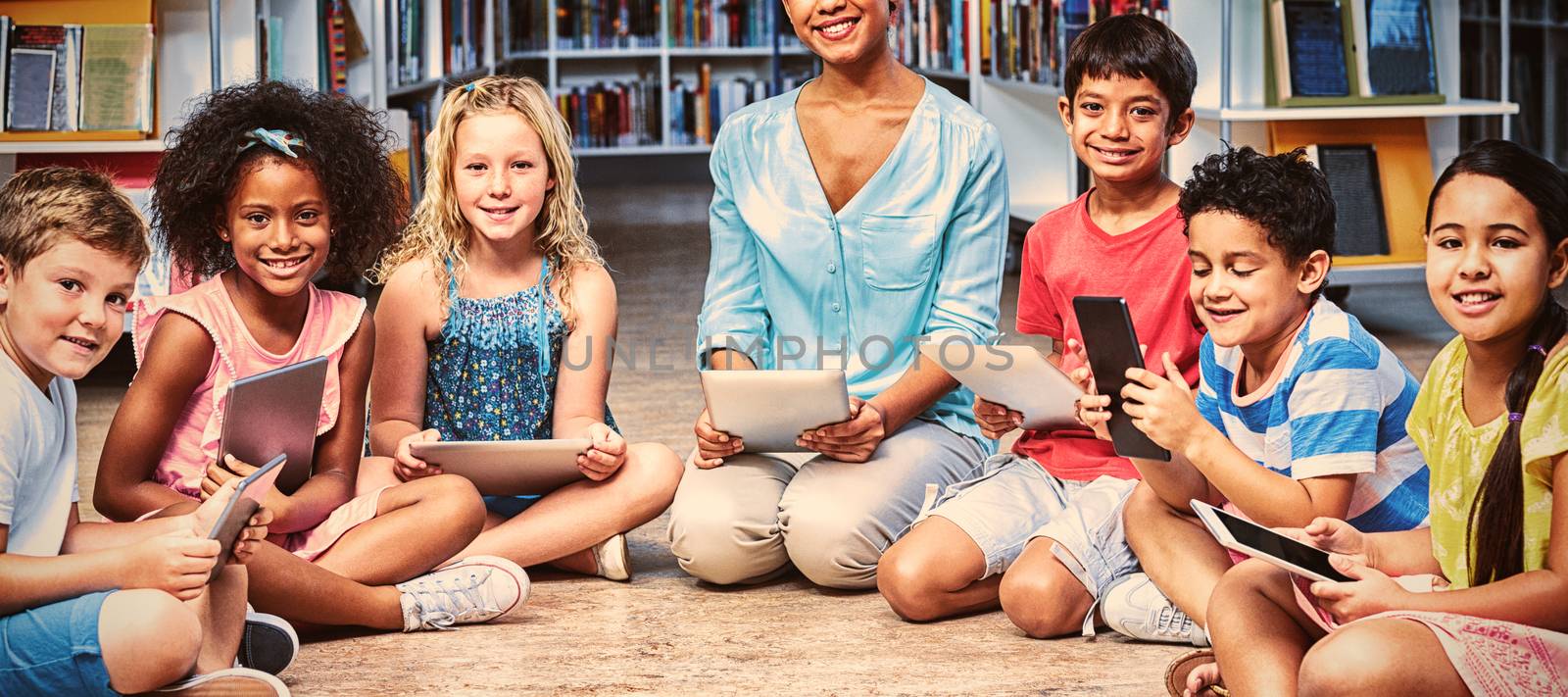 Portrait of female teacher with children holding digital tablets in library