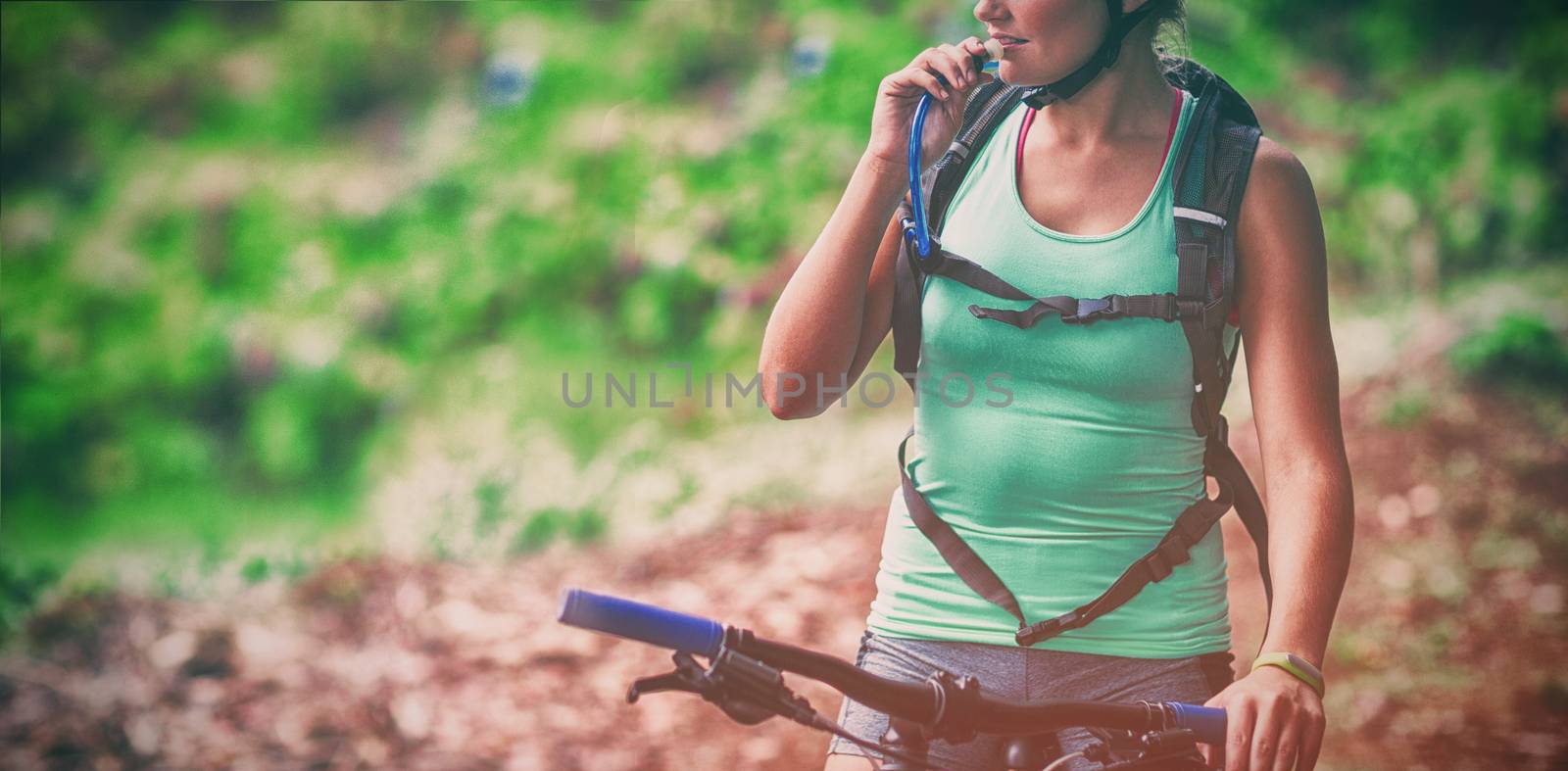 Female athletic drinking water from hydration pack in forest