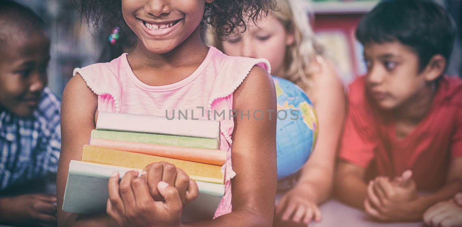 Portrait of smiling girl holding books against classmates in library