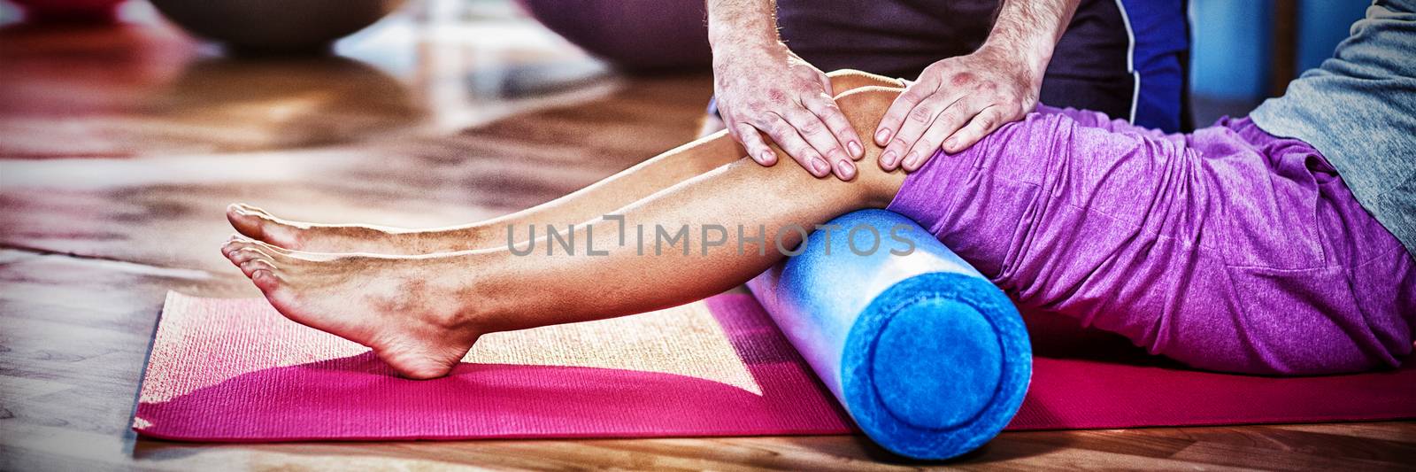 Midsection of physiotherapist assisting woman while exercising on exercise mat in clinic