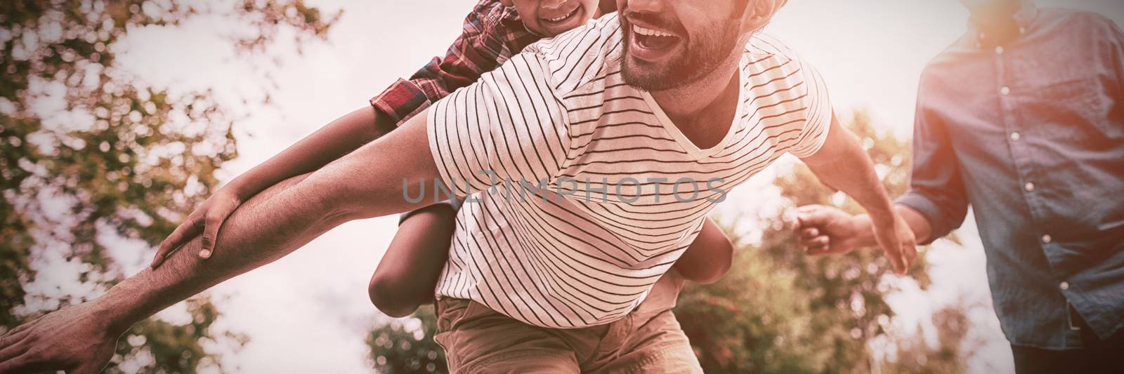 Happy grandfather looking at man giving piggy backing to son by Wavebreakmedia