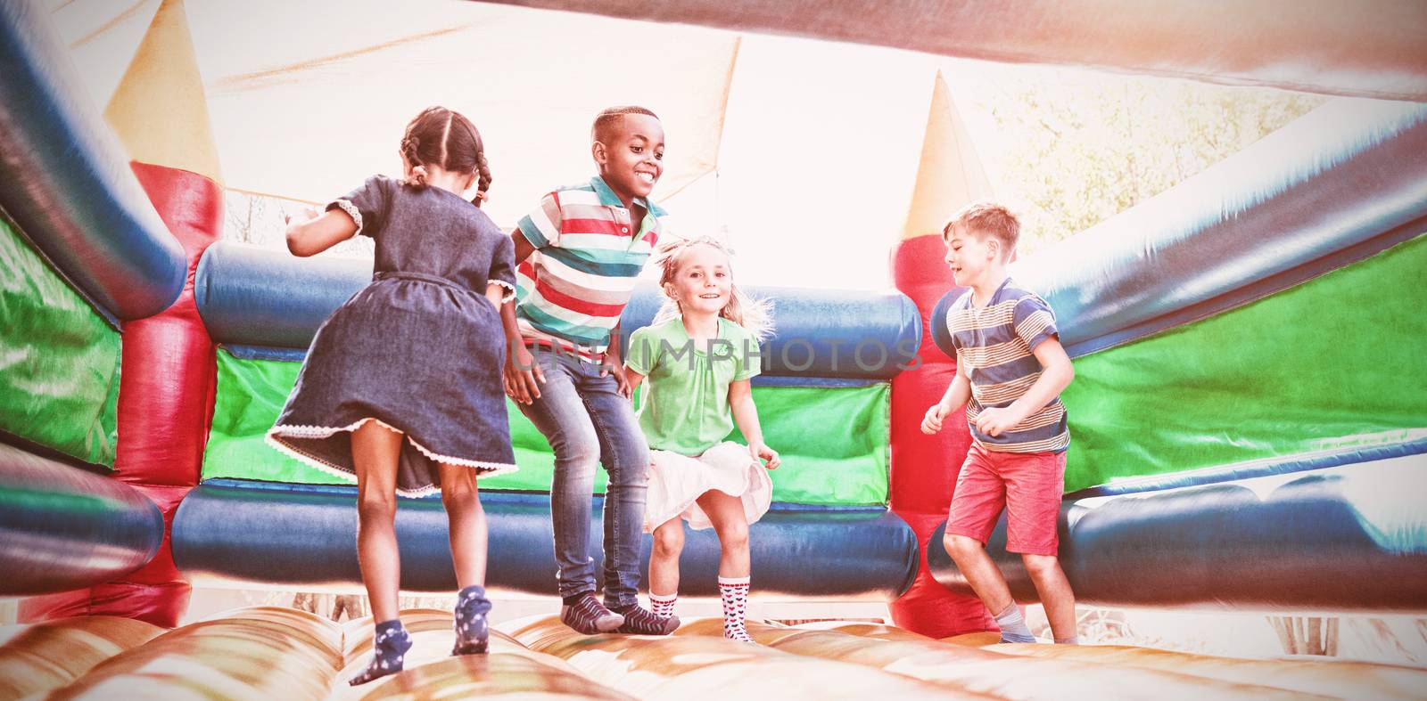 Full length of friends playing on bouncy castle at playground