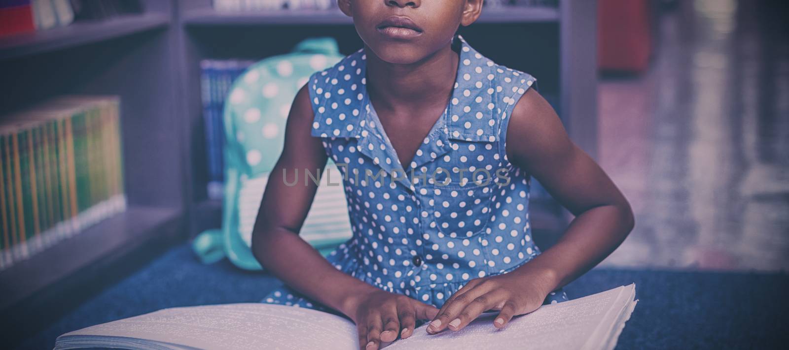 Girl reading braille book while sitting in library