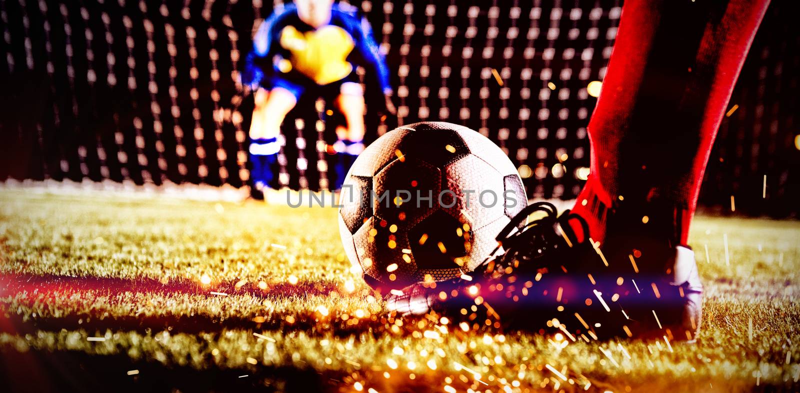 Low section of soccer player with ball against goalkeeper standing on playing field