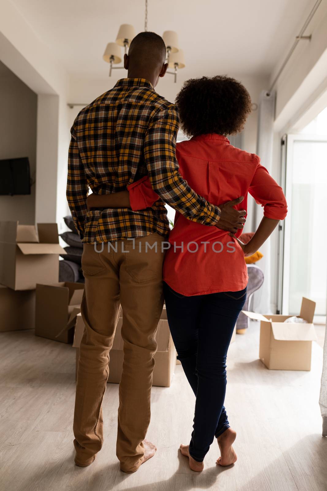 Rear view of African american couple standing together with arm around in living room at home