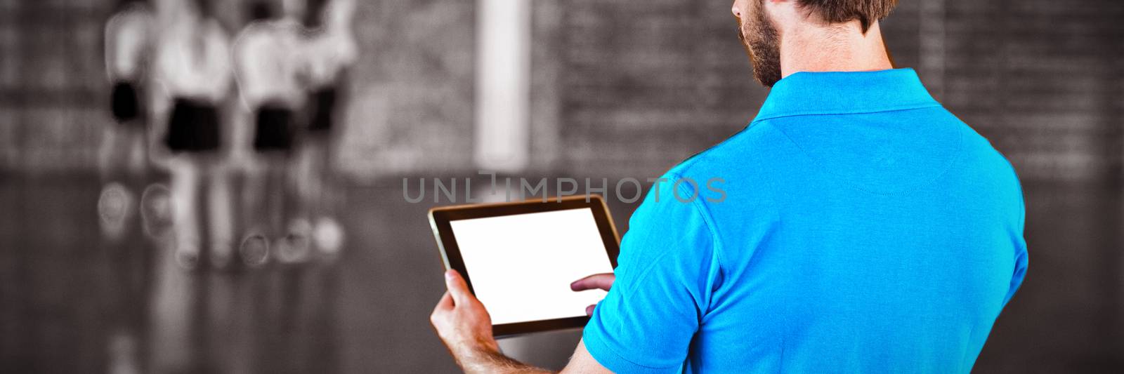 Male sports teacher using digital tablet in basketball court at school gym