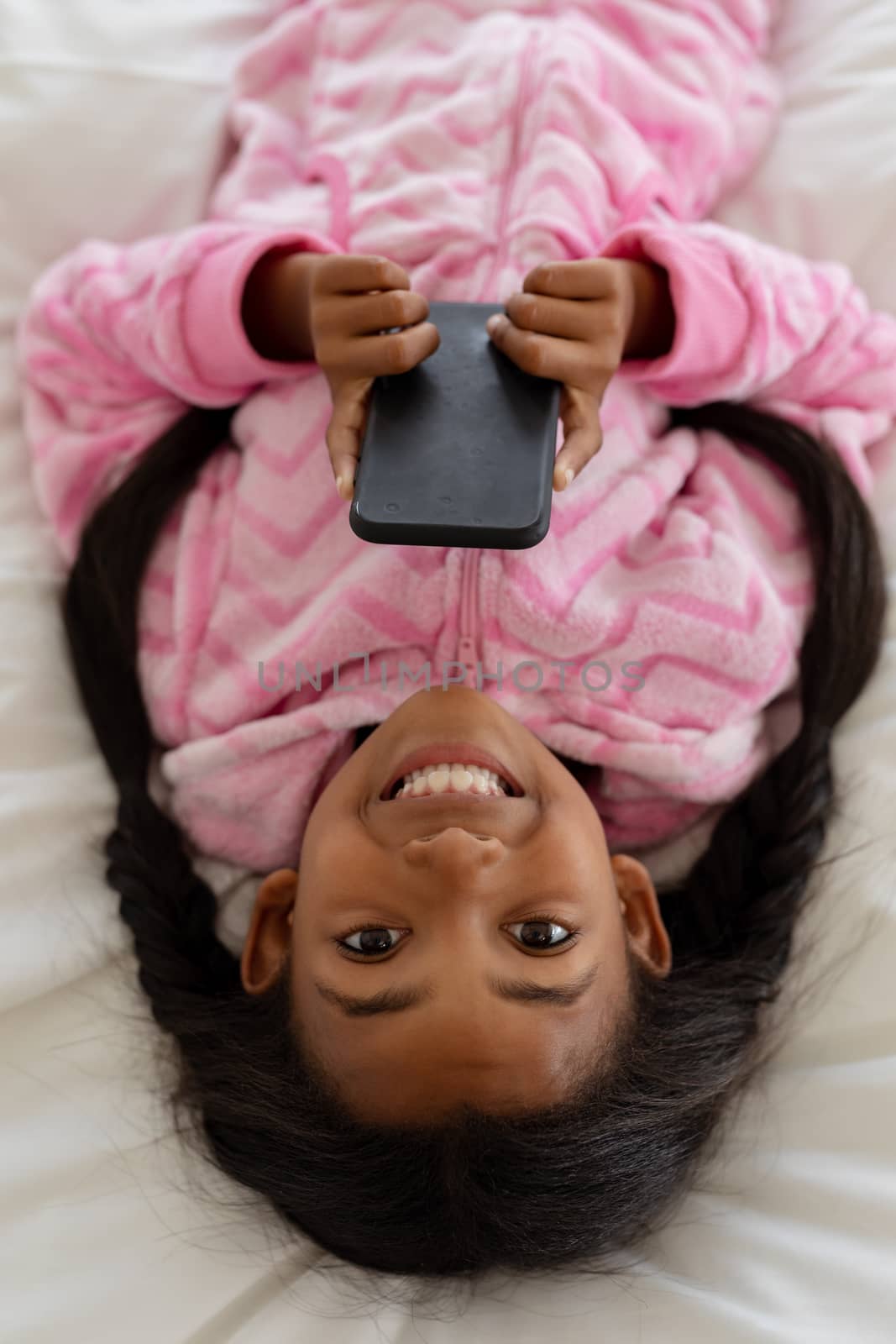 High angle view of African american girl using mobile phone while lying on bed in bedroom at home