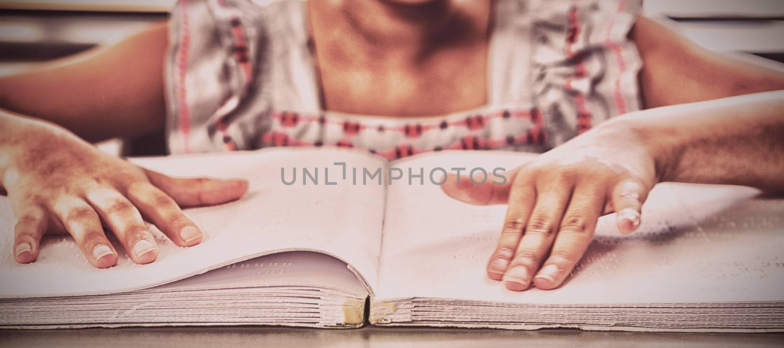 Midsection of blind girl reading braille book in classroom