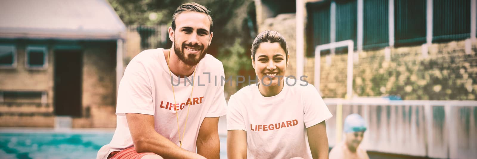 Portrait of male and female lifeguards holding rescue cans at poolside
