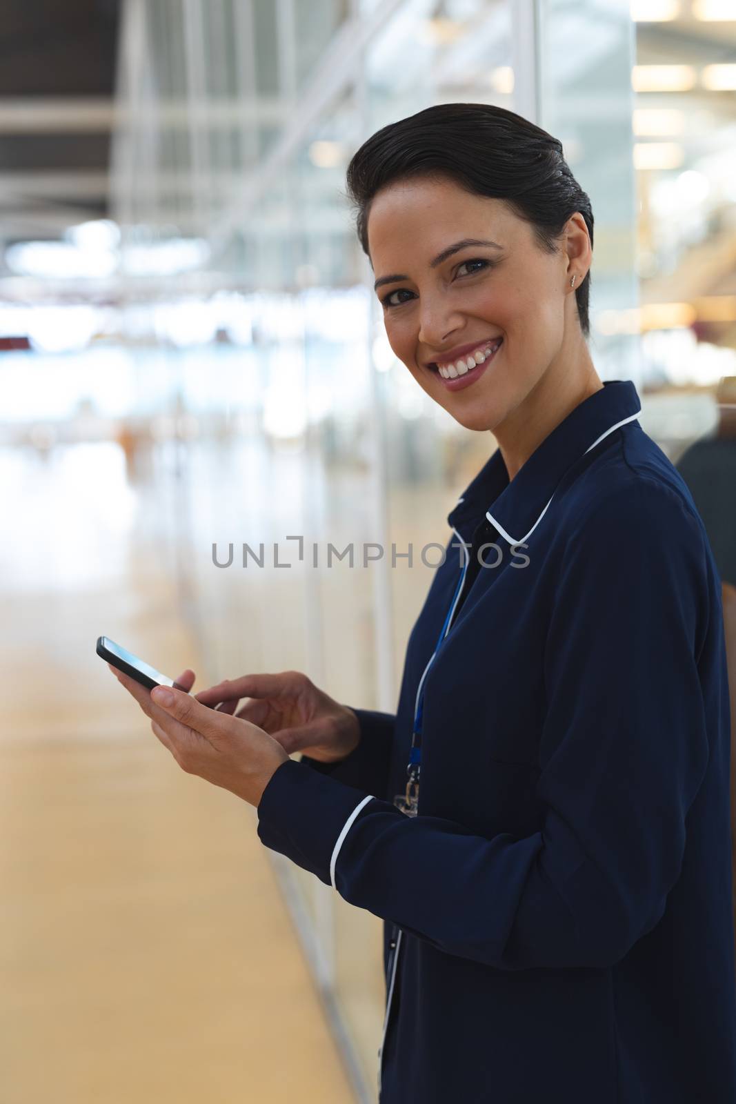 Portrait close-up of happy young Caucasian businesswoman looking at camera while using mobile phone in a modern office. International diverse corporate business partnership concept