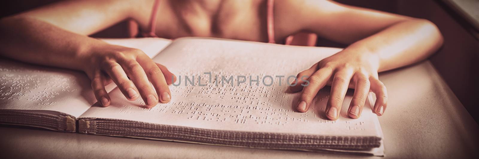 Blind girl using both hands to read braille in a room