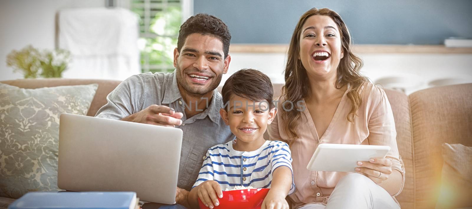 Son watching television while father and mother using laptop and digital tablet at home by Wavebreakmedia