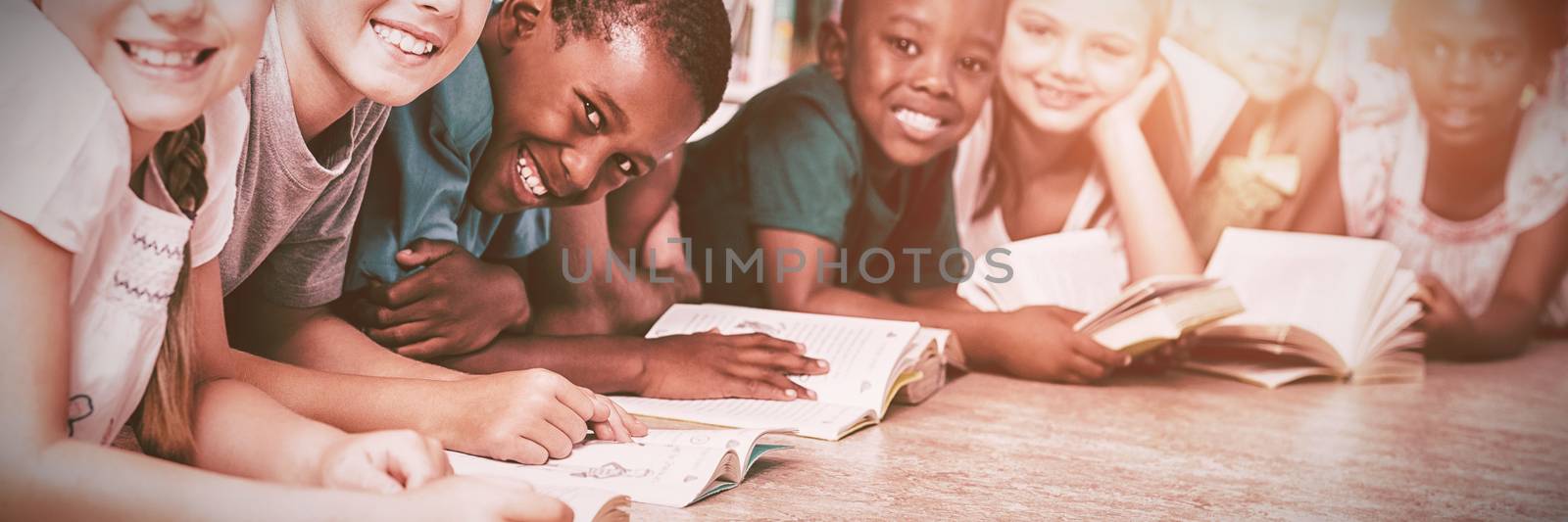 Teacher and kids lying on floor reading book in library at elementary school