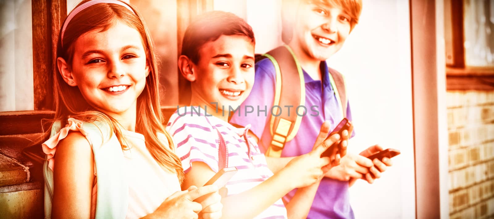 Portrait of school kids standing in corridor and using mobile phone at school