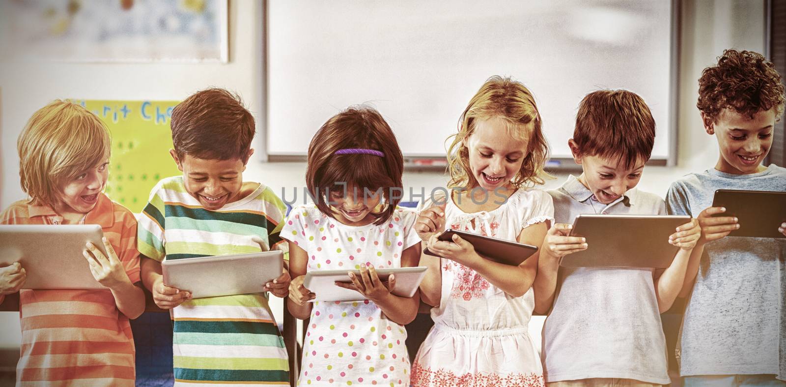 Smiling schoolchildren using digital tablets in classroom