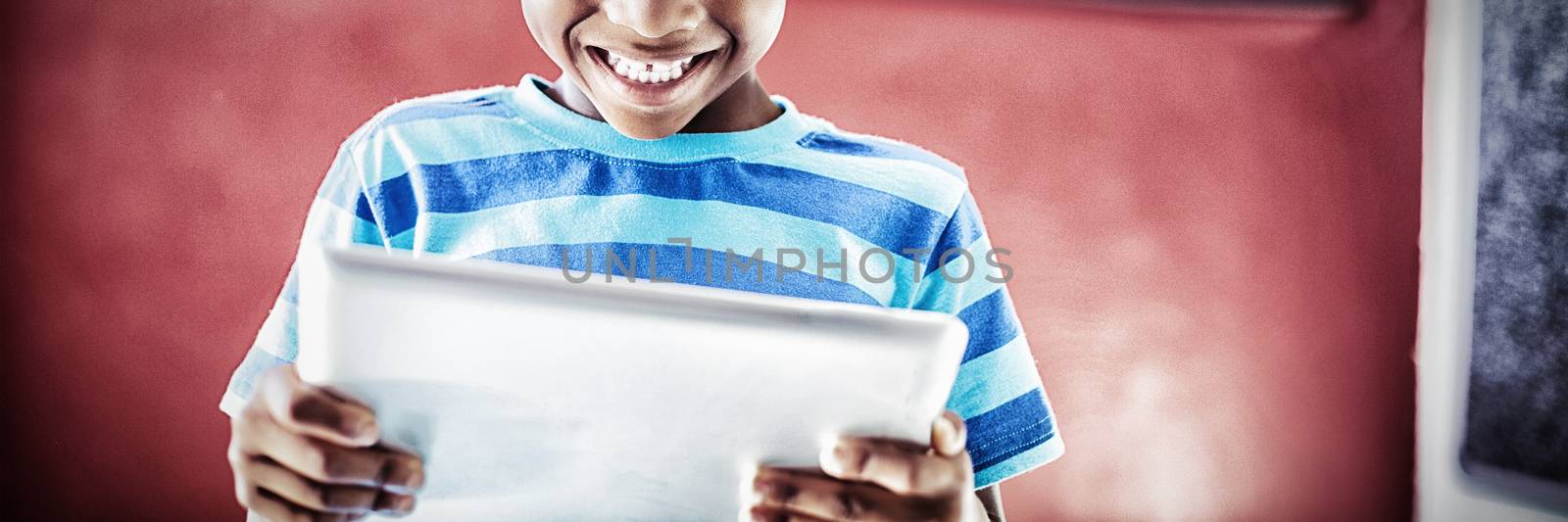 Happy schoolboy using digital tablet in classroom at school