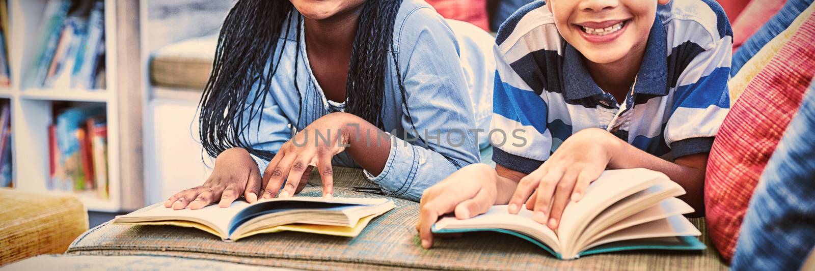 Portrait of school kids lying on sofa and reading book in library