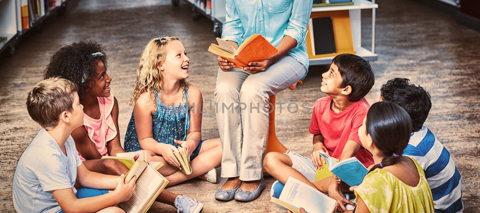 Happy female teacher with students reading books in library