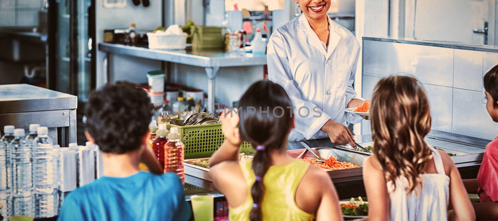 Smiling woman serving food to schoolchildren in canteen