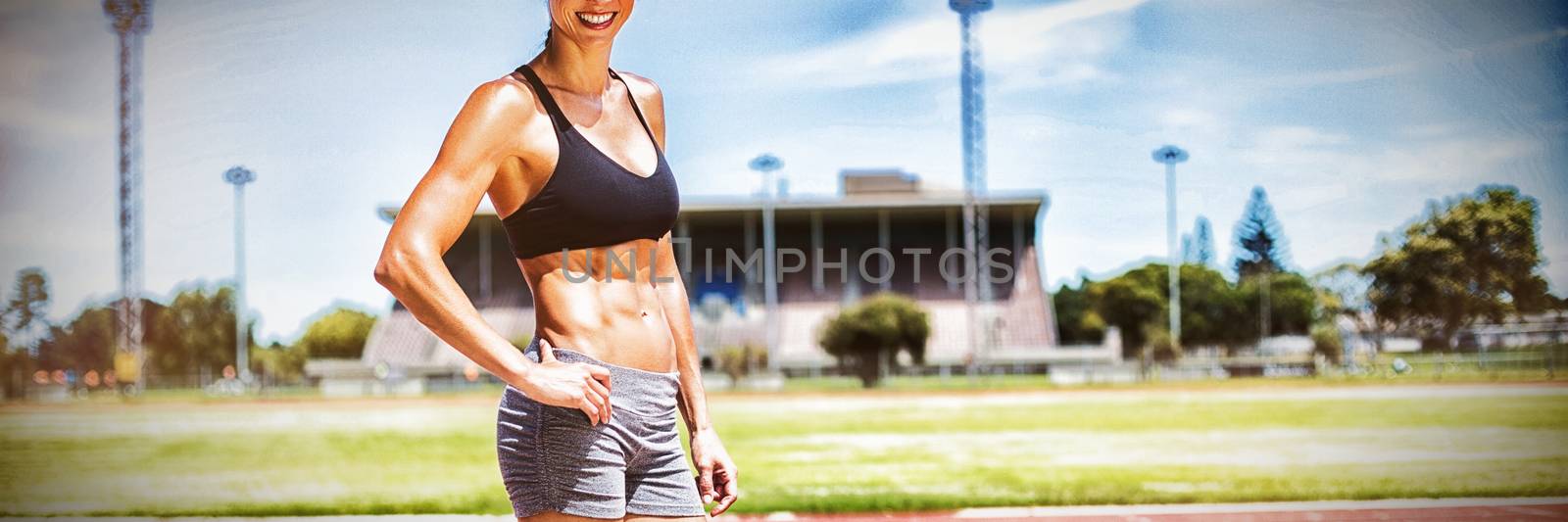 Portrait of female athlete standing in running track with hands on hips