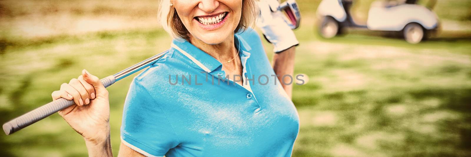 Portrait of happy mature woman carrying golf club while standing on field