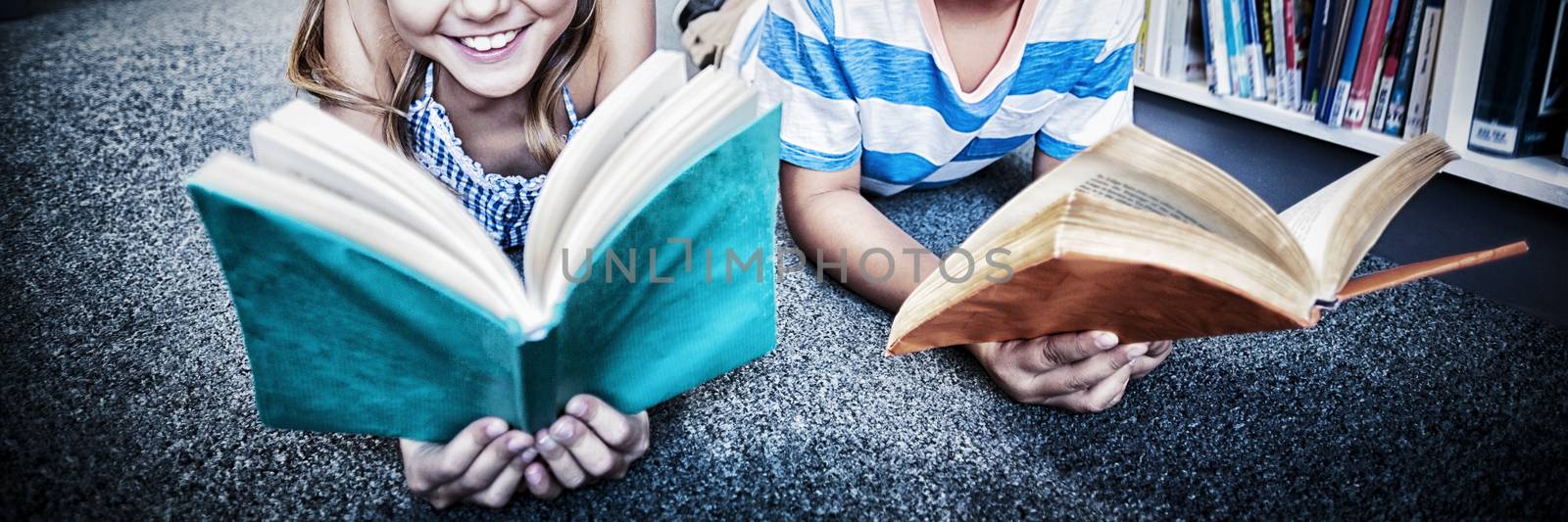 Portrait of happy school kids lying on floor and reading a book in library at school